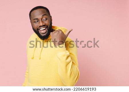 Side view of funny young man of African American ethnicity 20s wear casual basic yellow hoodie stand pointing thumb aside on mock up copy space isolated on pastel pink color background studio portrait Royalty-Free Stock Photo #2206619193