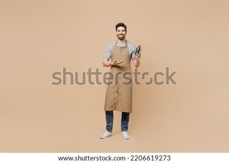 Full body young man barista barman employee wear brown apron work in bar pub nightclub hold shaker make alcohol cocktail isolated on plain pastel light beige background Small business startup concept Royalty-Free Stock Photo #2206619273
