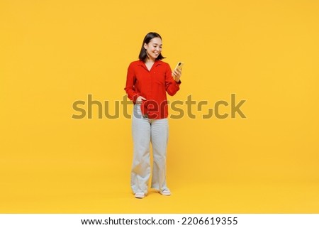 Full size body length vivid marvelous magnificent young woman of Asian ethnicity 20s years oldin casual clothes hold in hand use mobile cell phone isolated on plain yellow background studio portrait