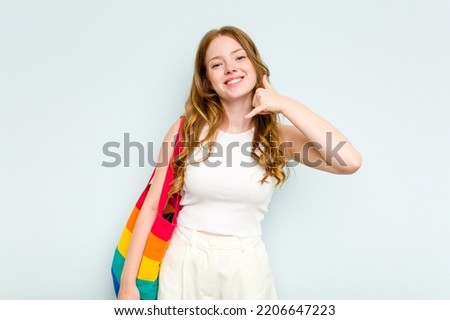 Young caucasian woman holding LGTBI bag isolated on blue background showing a mobile phone call gesture with fingers.