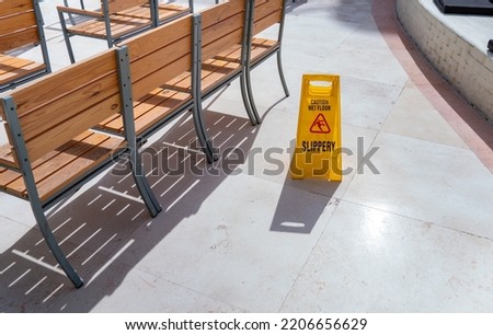 Safety sign with phrase Caution wet floor on road at the tropical resort. Cleaning service slippery