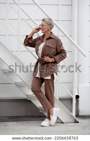 Fashionable woman stands. Short hair Model wears beige business suit with pants and jacket, belt purse, fashion accessories, loafers. Trend multilayered outfit. Fashion, style clothes Royalty-Free Stock Photo #2206658763