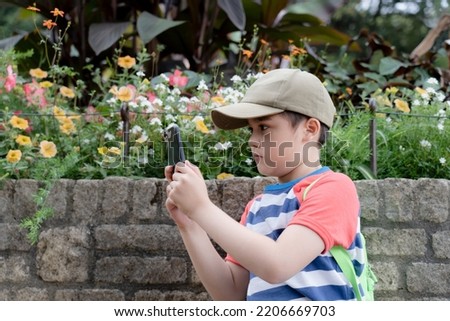 School kid using mobile phone taking photo of flowers in garden, Child boy learning about nature in the park, Happy kid having fun enjoying outdoor activities on warm summer day