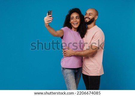 Black young man and woman taking selfie photo on cellphone isolated over blue background