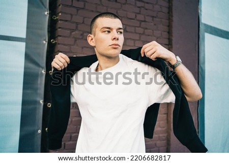 Candid waist portrait of a trendy handsome young man in city. Caucasian in early 20s man walking the street in urban setup. Looking away from camera. Casually dressed. Lifestyle Millenials. Short hair Royalty-Free Stock Photo #2206682817