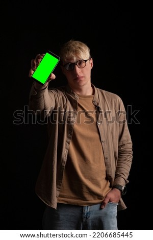 guy 23 years old holds in his hand a smartphone mockup with a chroma key screen on a black background