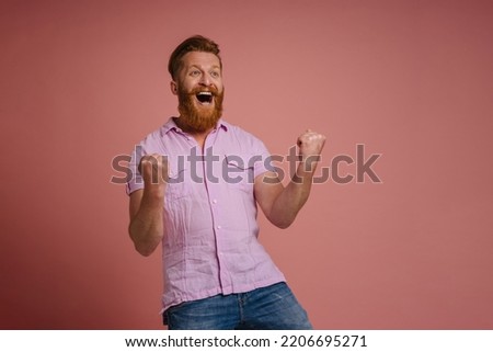 Ginger white man with beard screaming and winner gesture isolated over pink background