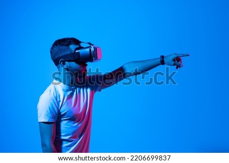 Young bearded man playing video games in VR-glasses. Excited millennial guy experiencing virtual reality while standing in neon light, copy space.