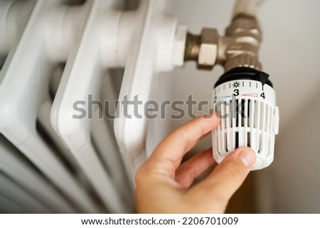 Rising heating costs in a crisis: people adjust the temperature in the house using a heating thermostat to save energy, close-up manually Royalty-Free Stock Photo #2206701009