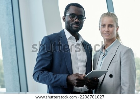 Portrait of two young intercultural office managers or business partners in elegant suits looking at camera while preparing presentation Royalty-Free Stock Photo #2206701027