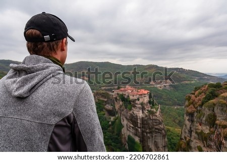 Selected focus on man with panoramic view of Holy Monastery of Varlaam, Kalambaka, Meteora, Thessaly, Greece, Europe. Rock formations overgrown with moss creating moody vibes. UNESCO World Heritage