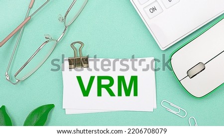 On a light green background there is a white calculator, a computer mouse, green leaves of a plant, gold-rimmed glasses and a white card with text VRM Vendor Relationship Management. Business concept