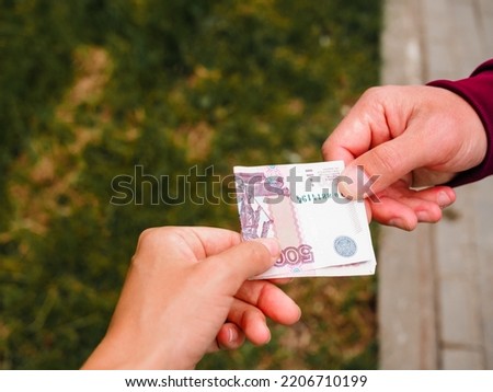 A man's and a woman's hand hold a bill of money