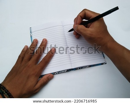 Hand of a person writing using a ballpoint pen on a notebook on a white background.