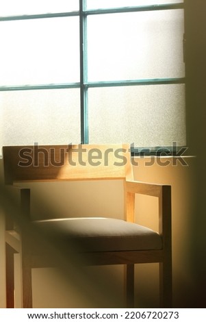 A comfortable wooden armchair in the room next to a window with sun rays and shadow on it