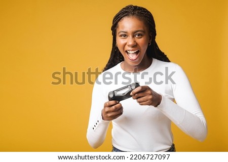 African american gamer woman playing video game using joystick over isolated yellow background. Very happy female looking to the camera