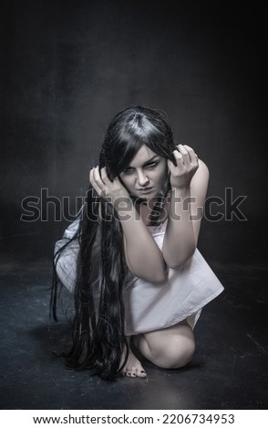 Mystical ghost woman with long black hair sitting on black background