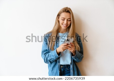 White blonde woman using mobile phone while standing by wall indoors