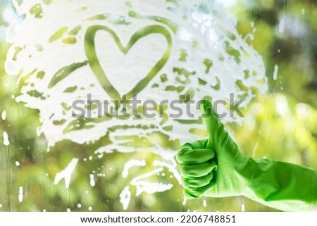 cleaning service concept. eco friendly detergent, good quality of service. window with heart shape foam and female hand in green glove showing thumb-up gesture