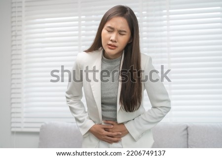 Flatulence, abdomen asian young business woman in suit at home, hand in stomach ache, expression face suffer from food poisoning, abdominal pain and colon problem, gastritis or diarrhoea, inflammation Royalty-Free Stock Photo #2206749137