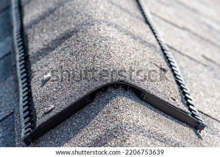 Ridge cap vent installed on a shingle roof for passive attic ventilation on a residential house.  Royalty-Free Stock Photo #2206753639