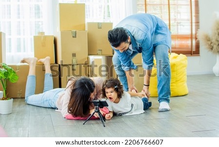 Happy family with three members Caucasian father, Asian mother and little daughter laughing, playing together, selfie, taking photo by mobile phone with fun and happiness while moving to new house