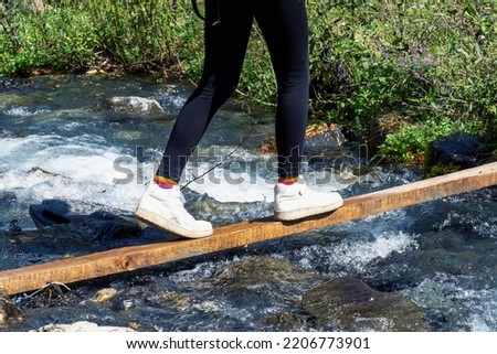 A young girl crosses a mountain river on a plank