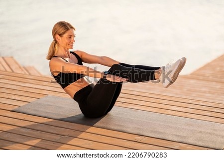 Athletic Middle Aged Woman Making V-Up Abs Workout Outdoors, Sporty Smiling Woman Training On Wooden Pier Near River, Exercising On Fitness Mat Outside, Enjoying Healthy Lifestyle, Copy Space Royalty-Free Stock Photo #2206790283