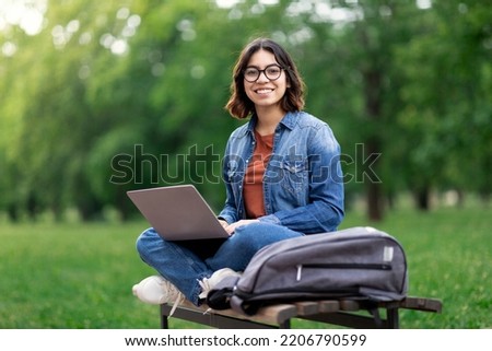 Portrait Of Happy Middle Eastern Female Student Sitting On Bench Outdoors With Laptop, Beautiful Young Arab Woman Using Computer In Park, Enjoying Online Education And Distance Learning, Copy Space Royalty-Free Stock Photo #2206790599