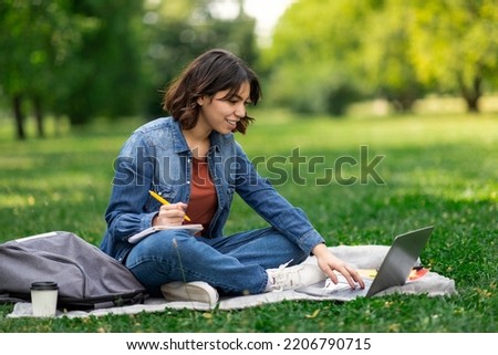 Young Middle Eastern Woman Study Outdoors With Laptop And Notepad Study Outdoors, Smiling Arab Female Student Preparing For Exam Outside, Sitting On Lawn In Park, Enjoying Online Education Royalty-Free Stock Photo #2206790715