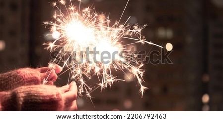 Hand holding sparkler. Sparkler with blurred busy city light background. Festive sparklers at night.