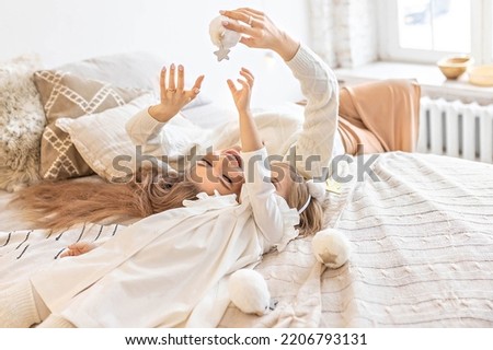 Mom and daughter play with fluffy soft snowballs, lying on the bed in a bright bedroom.Family. Ethno-interior design