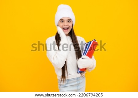 Excited face. Winter school. Teenager school girl with books in autumn clothes on yellow isolated studio background. Amazed expression, cheerful and glad.