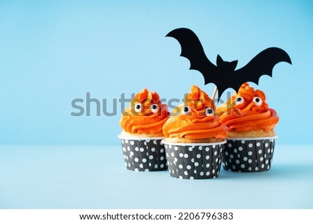 Monster orange funny cupcakes with eyes and bat on blue background, copy space