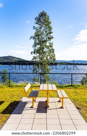 Warm July in Norway. Picnic table and benches by the lake. Cozy corner for tourists. Light white clouds in the blue sky illuminated by the sunrise. Magical summer morning.