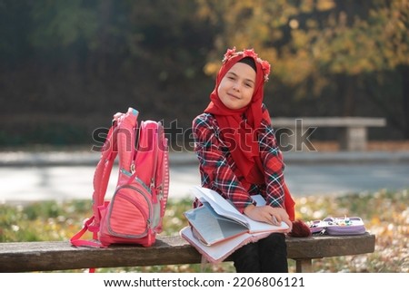 A happy Muslim girl student learning for school in the autumn park.