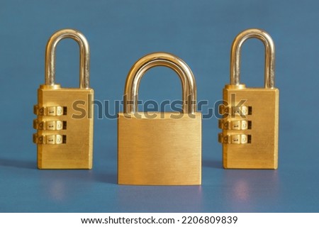 A golden square padlock escorted by two rectangular combination padlocks s in the background on a blue-painted study table. Leadership and security concept.
