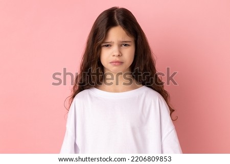 Portrait of upset little girl wearing white T-shirt expressing negative emotions and sorrow, has bad mood, being sad and unhappy. Indoor studio shot isolated on pink background. Royalty-Free Stock Photo #2206809853