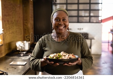 Front view of an Senior African woman at a cookery class, holding a bowl filled with vegetables. Active Seniors enjoying their retirement. Royalty-Free Stock Photo #2206816361