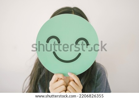 Happy mixed Asian girl holding smile emoji face, positive mental health concept Royalty-Free Stock Photo #2206826355