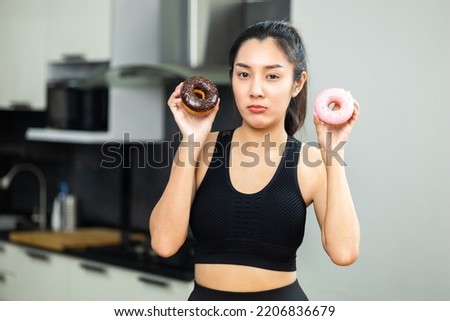 Beautiful female in sportswear eating Sweet donut dessert. Hungry Young woman holding chocolate donut unhealthy food. Food and dessert concept.