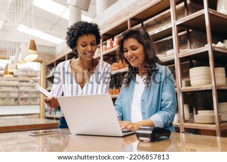Happy young ceramists using a laptop while working in their store. Female entrepreneurs managing online orders on their website.Cheerful young businesswomen running a creative small business together.