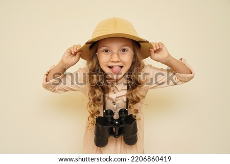 Child discoverer.  Unique child.  Traveler child.  Young travel blogger.  Little cute girl in a fashionable suit and hat for trips to Safari with binoculars in her hands.  Trendsetter. Royalty-Free Stock Photo #2206860419
