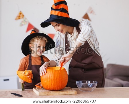 Cute happy little boy helping his mother to carve Halloween pumpkin  at home and preparing for autumn holiday, family son and mom making Jack-o-Lantern together