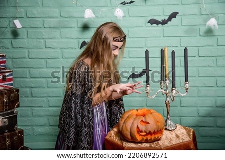 Halloween children, Girl with a witch costume conjures over a pumpkin. Halloween carnival, holiday costumes for fun at home.