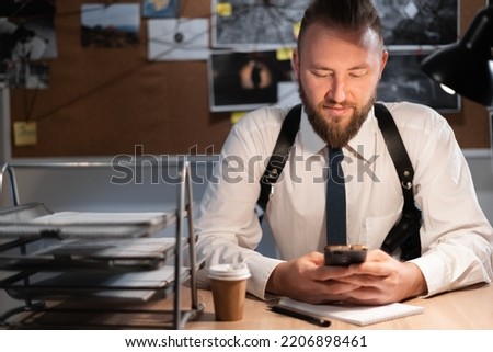 A male detective is sitting in the office flipping through the news feed. A detective board with photos, a map and clues connected by a thread on the wall. copy space.
