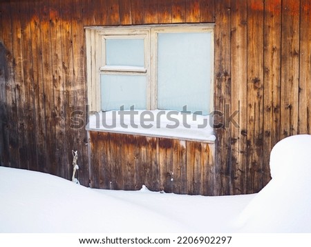 Frozen hut window in winter. Frost on glass. Snow and snowdrifts. Wooden wall of the house. Rural illustration on winter theme