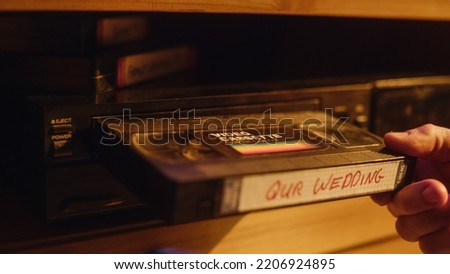 Close Up of a Person Inserting a VHS Cassette in a Player with Nostalgic Wedding Footage from Home Video Camera. Retro Nineties Technology Concept. Old VCR with Shallow Depth of Field and Bokeh. Royalty-Free Stock Photo #2206924895