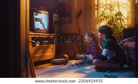 Nostalgic and Happy Childhood Concept: Young Brother and Sister Playing 8 Bit 2D Arcade Video Game on a Retro TV Set at Home in a Room with Period-Correct Interior. Friends Completing the Level.