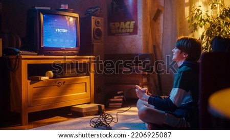 Young Boy Playing 80s Eight Bit Arcade Space Shooter Video Game on a Console at Home in His Vintage Room with Old-School Interior. Child Successfully Wins the Level. Nostalgic Retro Childhood.